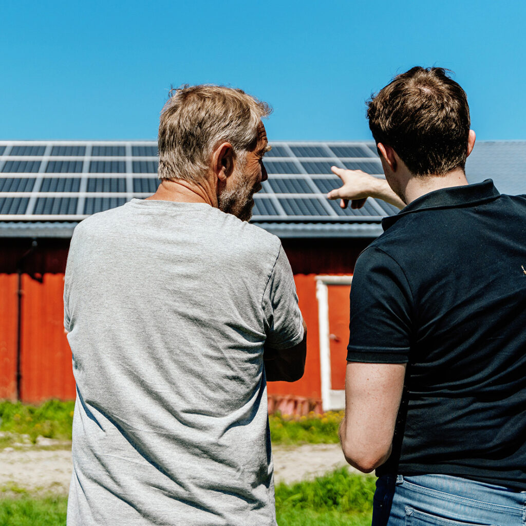 To menn som snakker om og peker på solcelleanlegg på låvetaket